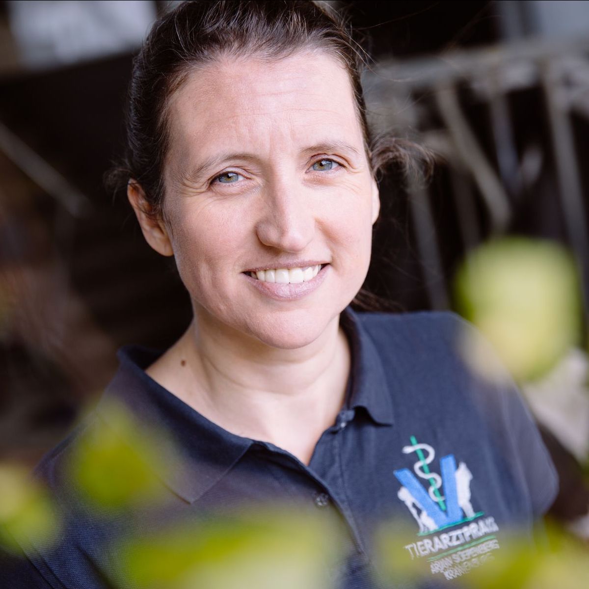 Frau in dunkelblauem Polohemd lächelt, mit Tierarzt-Emblem, im Freien.