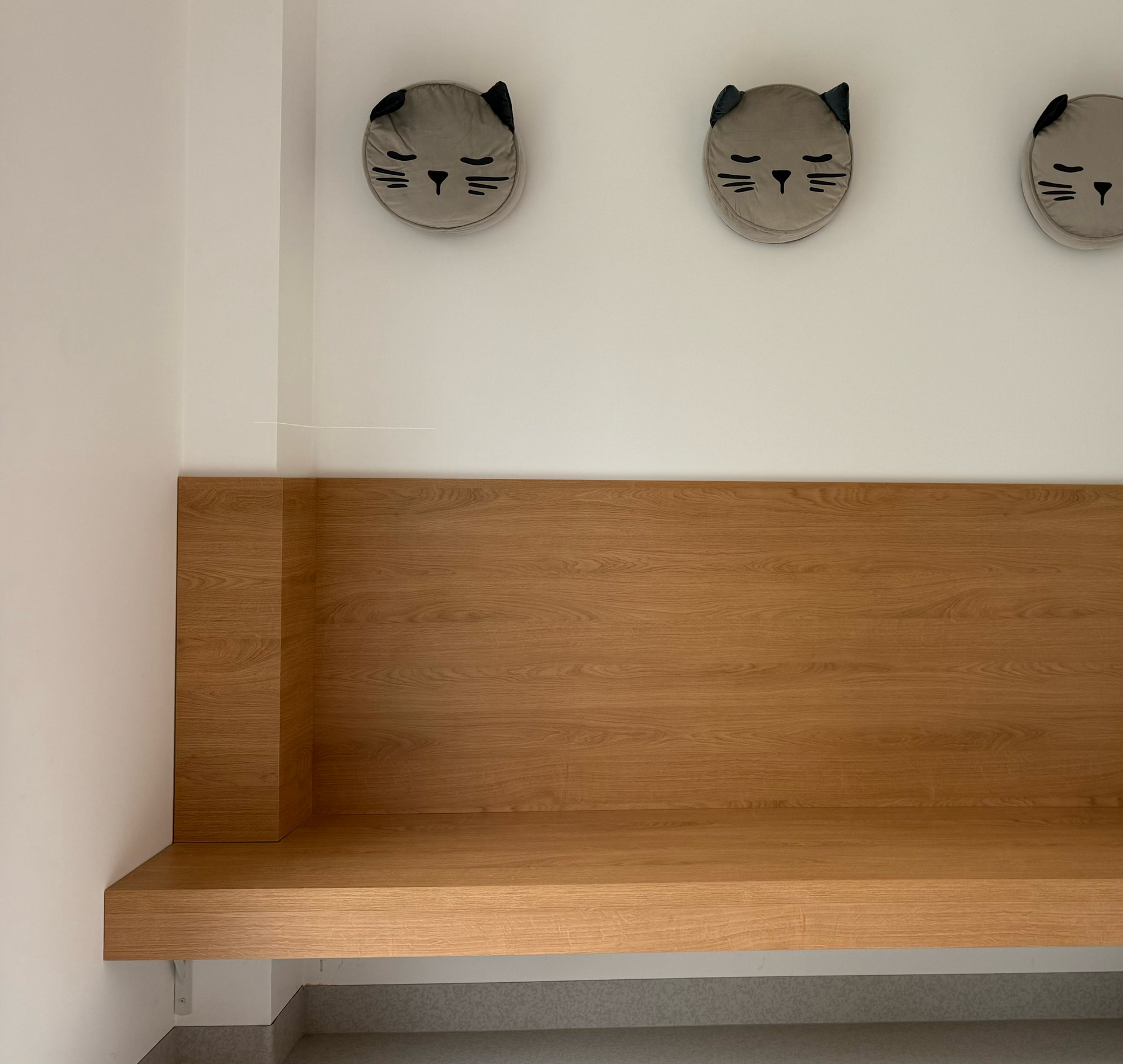 Eine Holzbank unterhalb von drei katzenförmigen Wanddekorationen an einer weißen Wand.