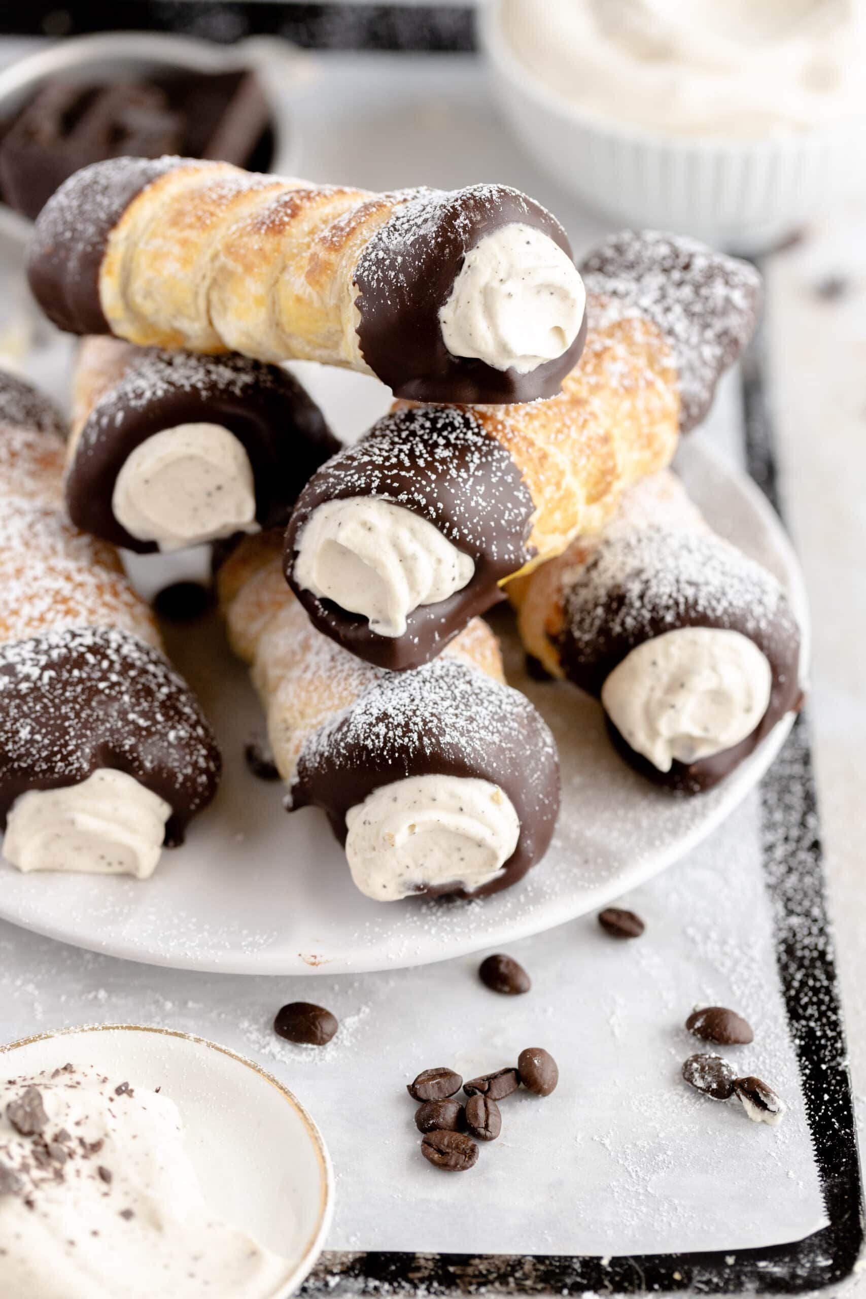 Cannoli pastries, chocolate dipped, filled with cream, dusted with powdered sugar, on a white plate.