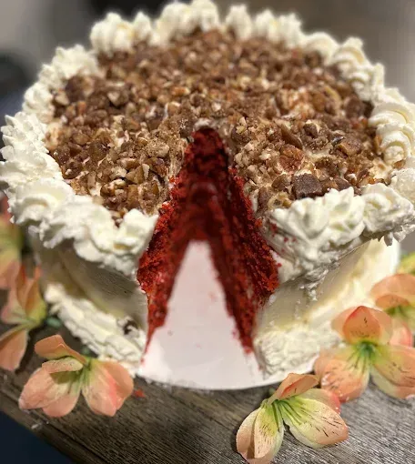 Red velvet cake with white frosting and topping, cut to show layers, with flowers.