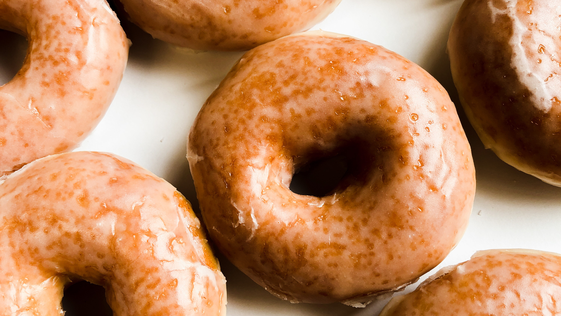 Glazed donuts, golden brown with a glossy sheen, arranged closely on a white surface.