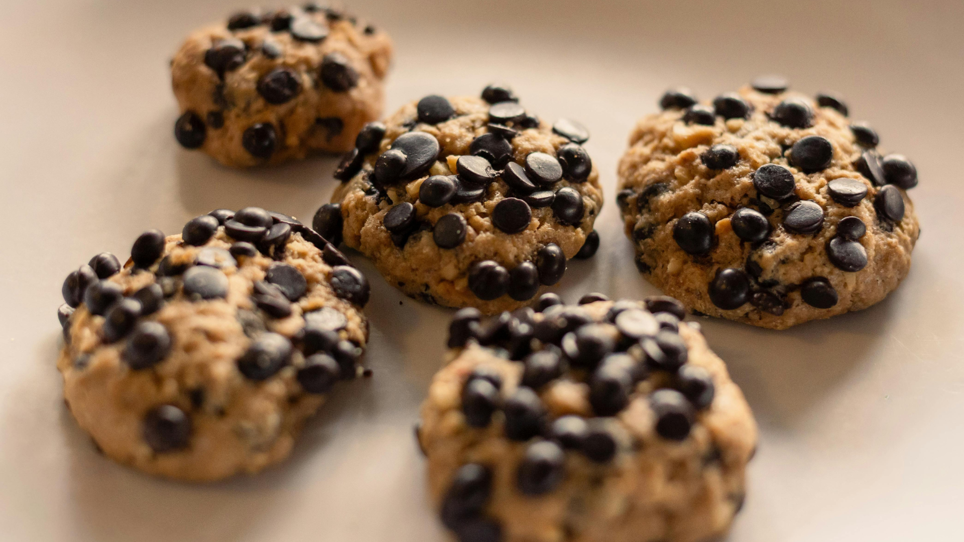 Five chocolate chip cookies on a white plate.