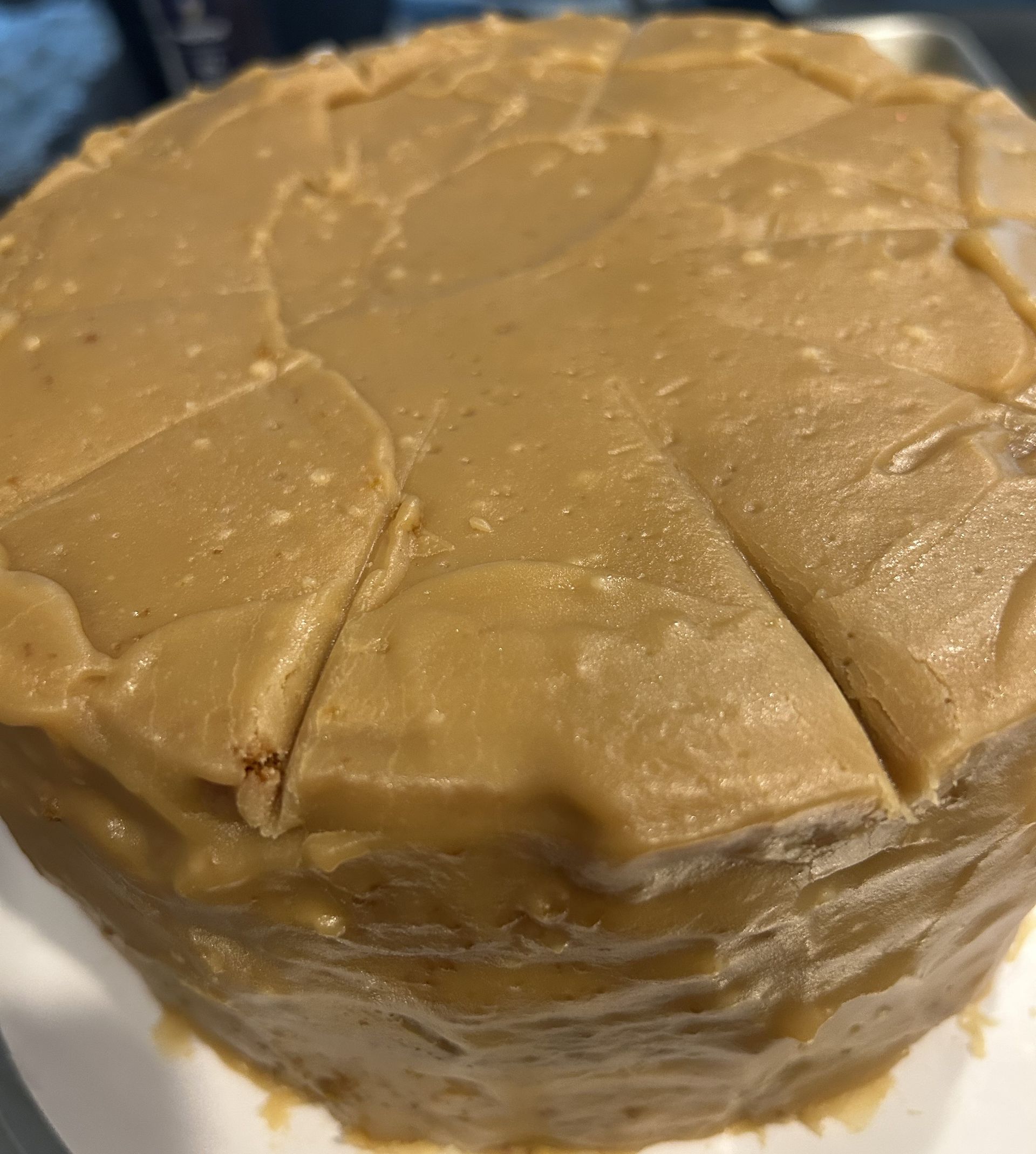 Round cake with tan frosting, pre-cut into pie-like slices.