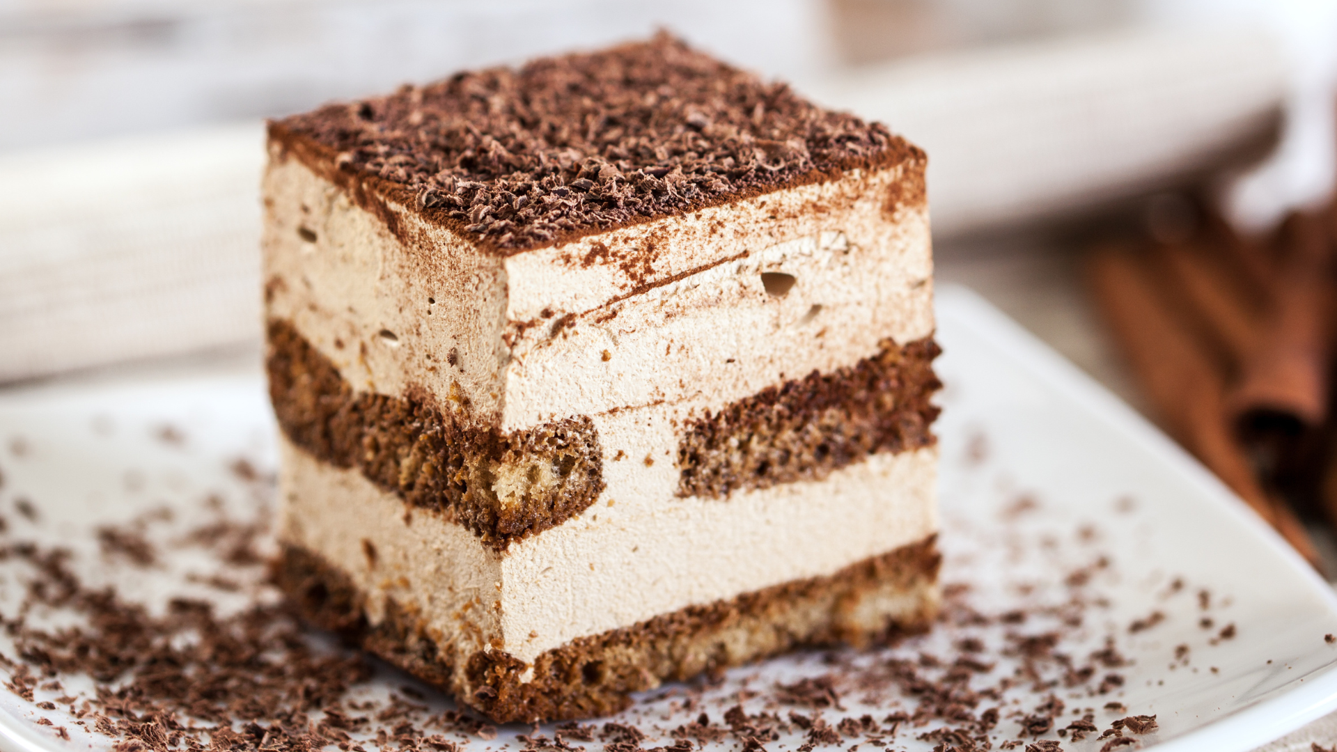 Tiramisu dessert, layered with creamy filling and cocoa powder, on a white plate.