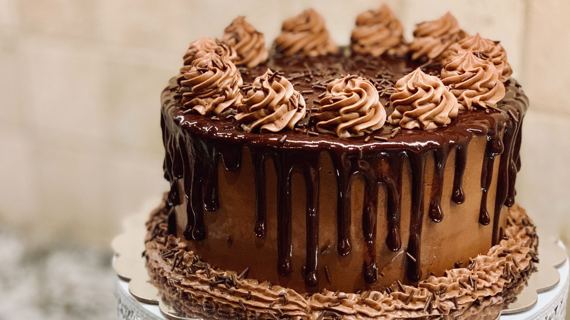 Chocolate cake with chocolate frosting, drip, and swirls on a white cake stand.
