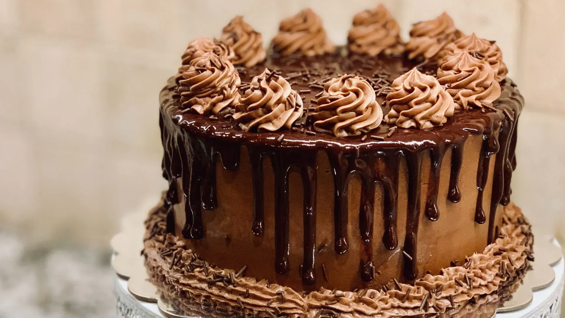 Chocolate cake with chocolate frosting, drip, and swirls on a white cake stand.