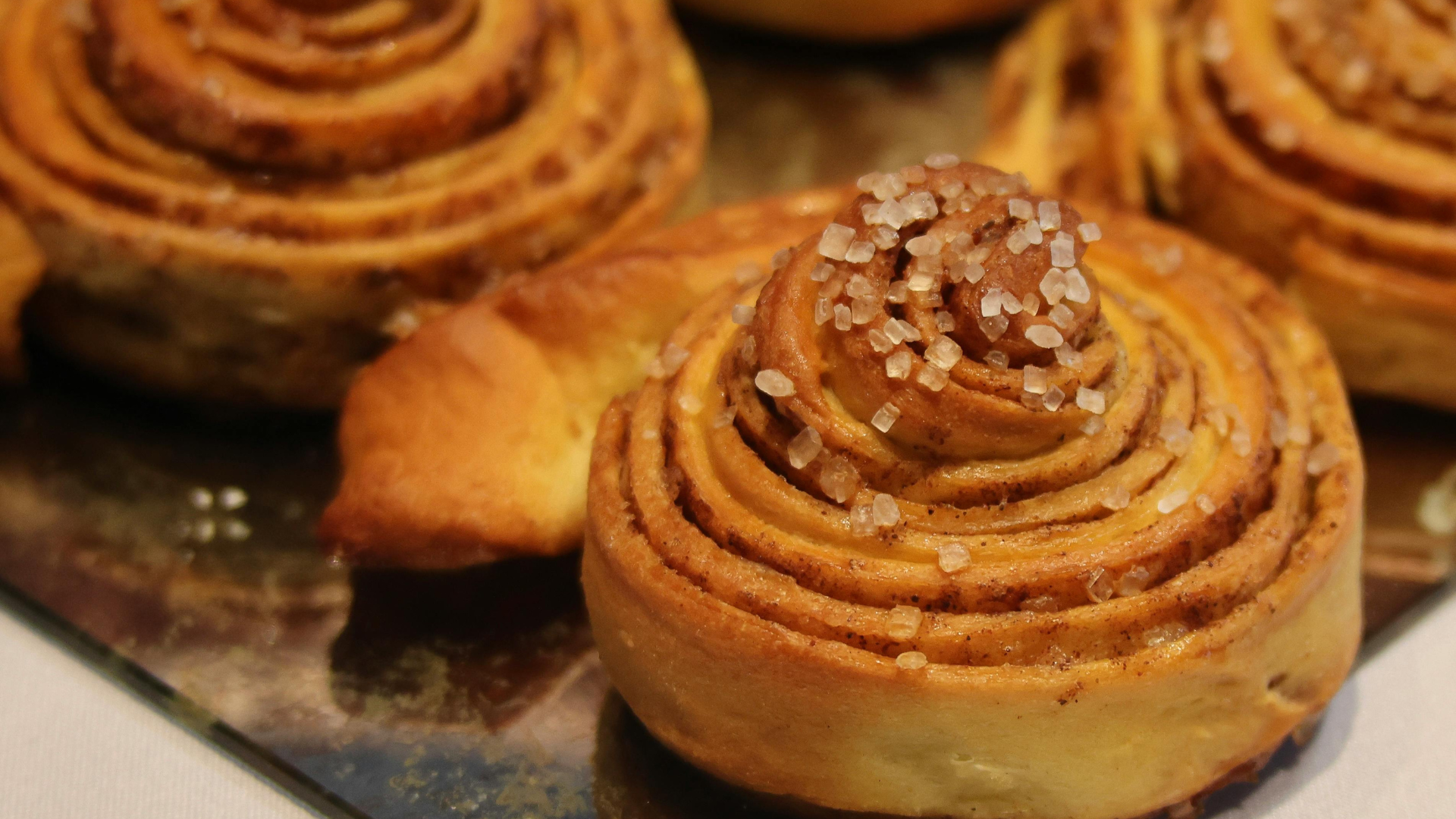 Close-up of baked cinnamon rolls with sugar crystals on a metallic tray.