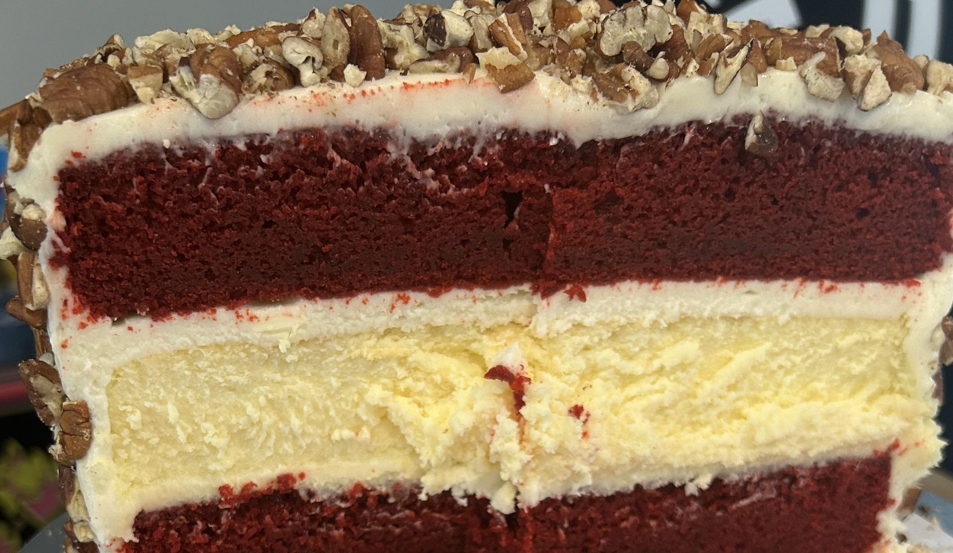 Cross-section of red velvet cake with cheesecake layer and pecan topping.