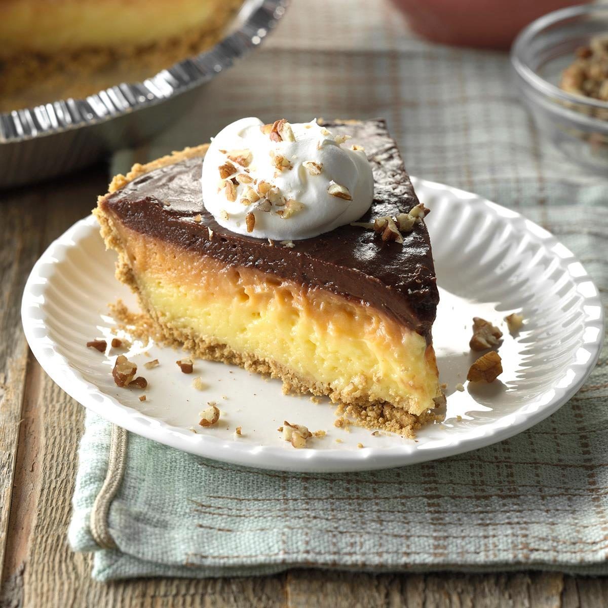 Slice of chocolate cream pie on white plate, topped with whipped cream and nuts.