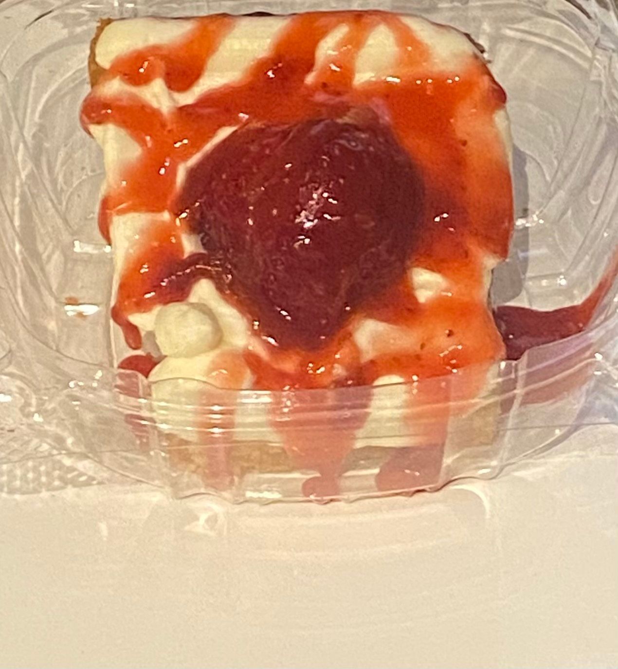 Strawberry cheesecake slice in clear plastic container.