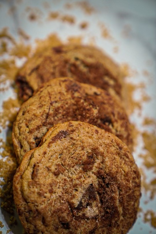 Three cinnamon-sugar cookies on a surface dusted with brown sugar.