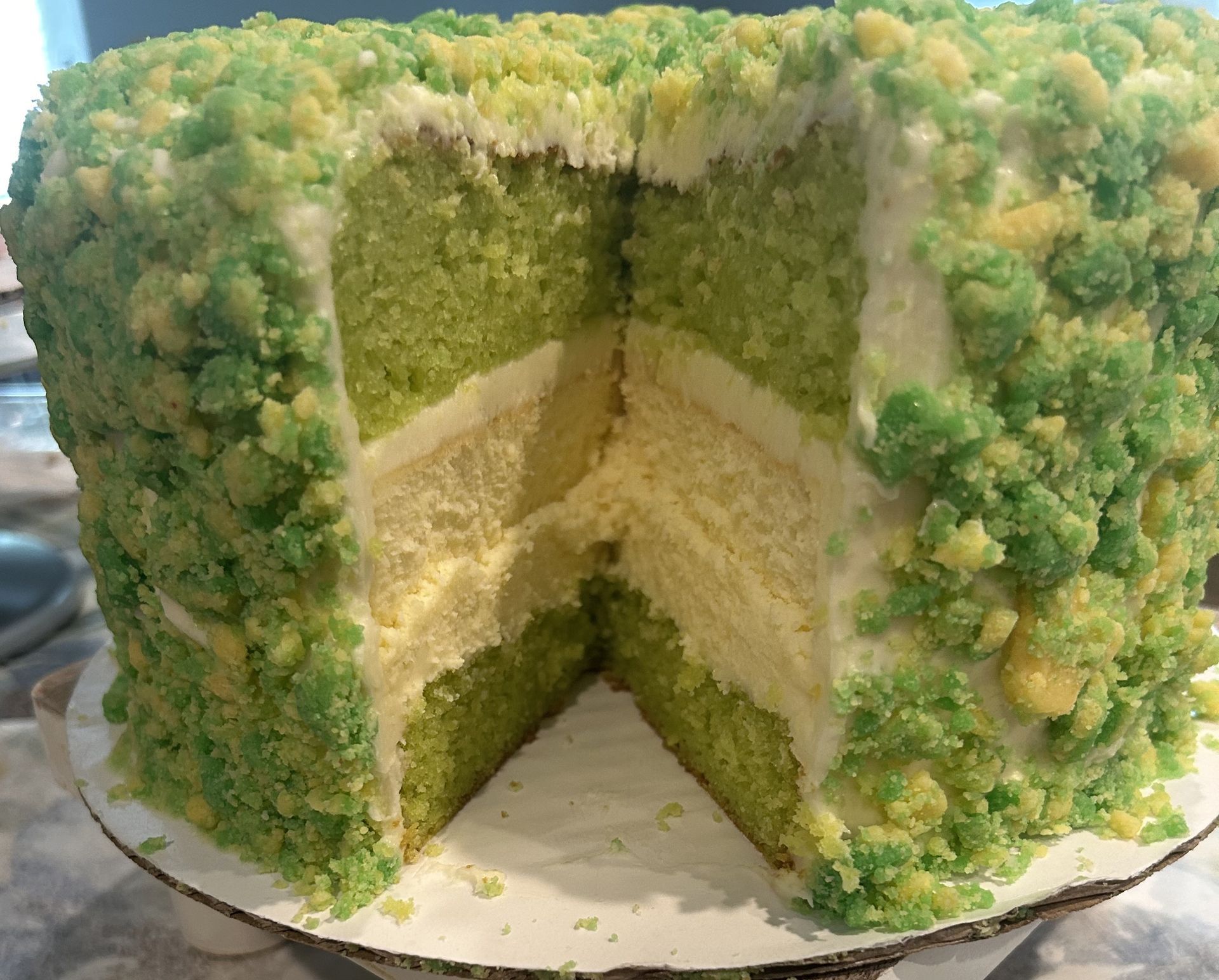 Green and white layered cake with a crumb coating, cut open to show layers.