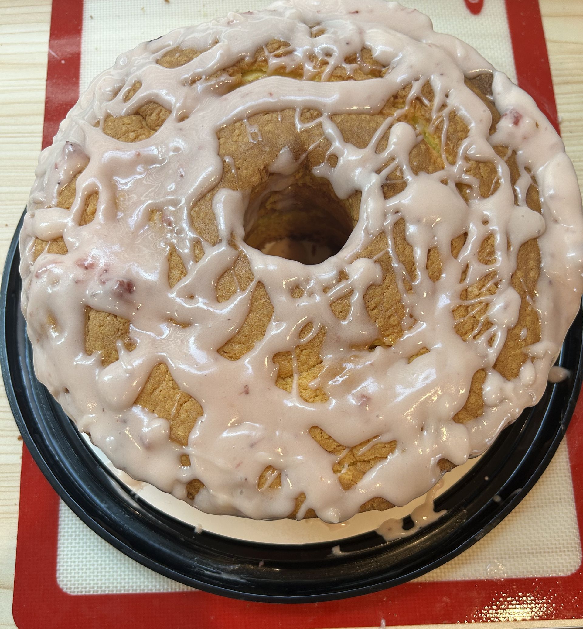 Bundt cake with pink glaze on a silicone baking mat.