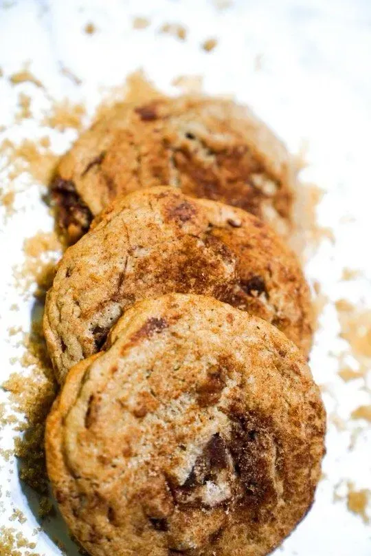Three cinnamon swirl cookies on a white surface with scattered brown sugar.