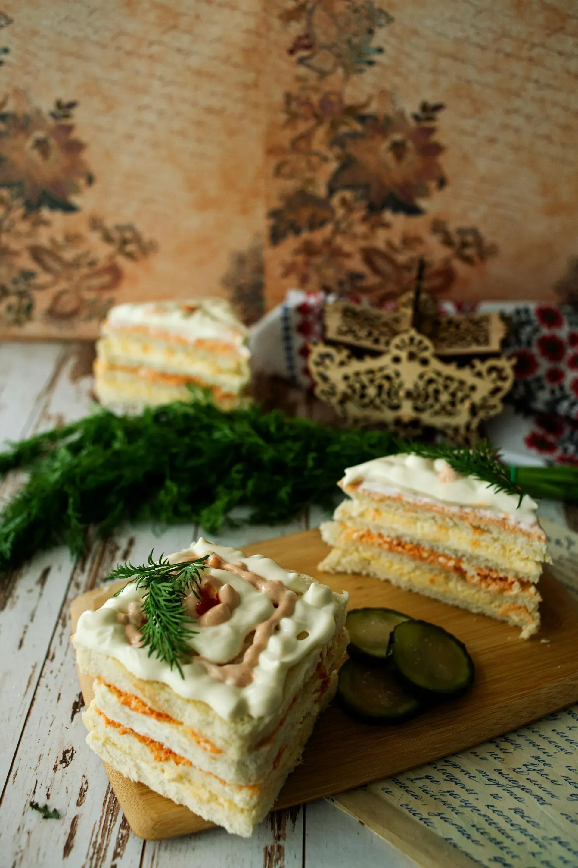 Slices of savory cake with white frosting, orange filling, and dill garnish, on a wooden board.