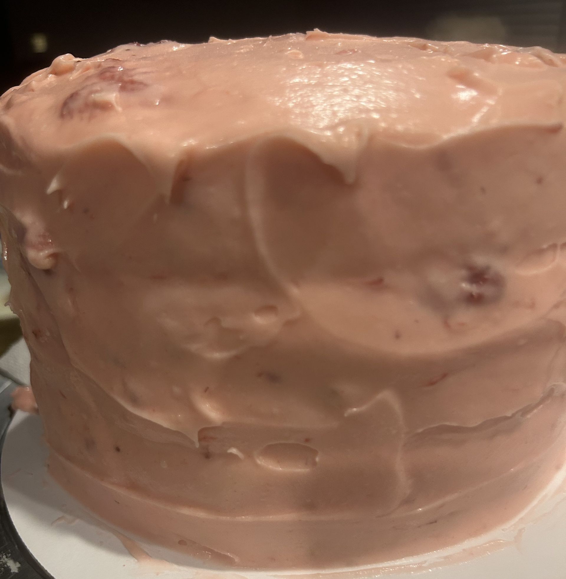 Pink frosted cake on a white plate, with visible strawberry pieces in the frosting.