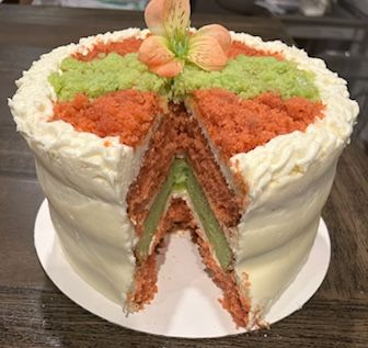 Cake with white frosting, orange and green crumb toppings, and a flower on top. A slice is cut.