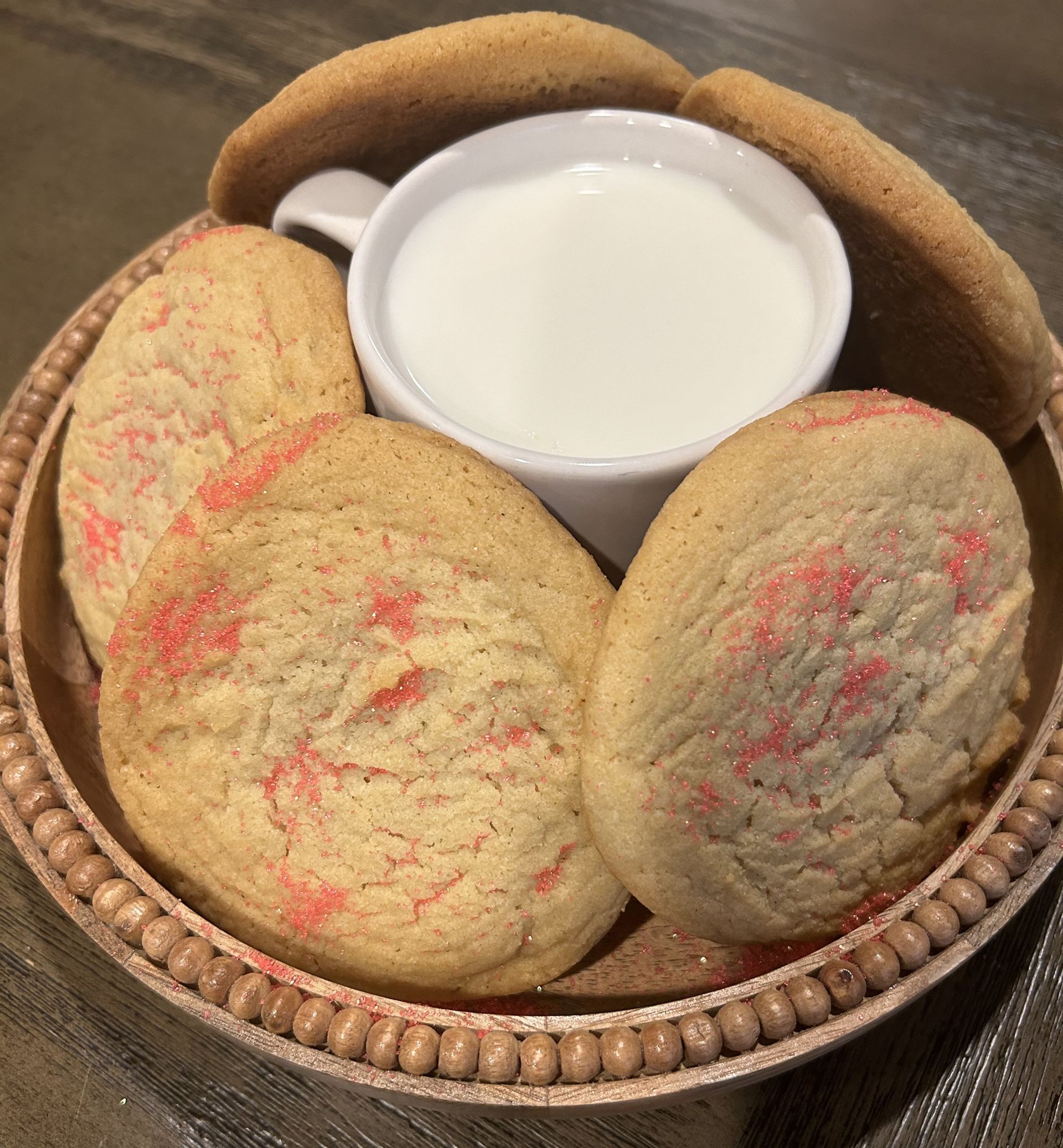 Cookies with red sprinkles and a cup of milk on a decorative plate.