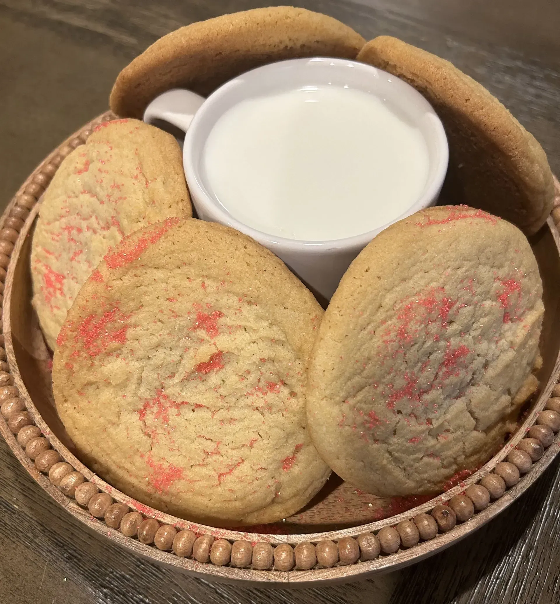 Cookies with red sprinkles and a cup of milk on a decorative plate.