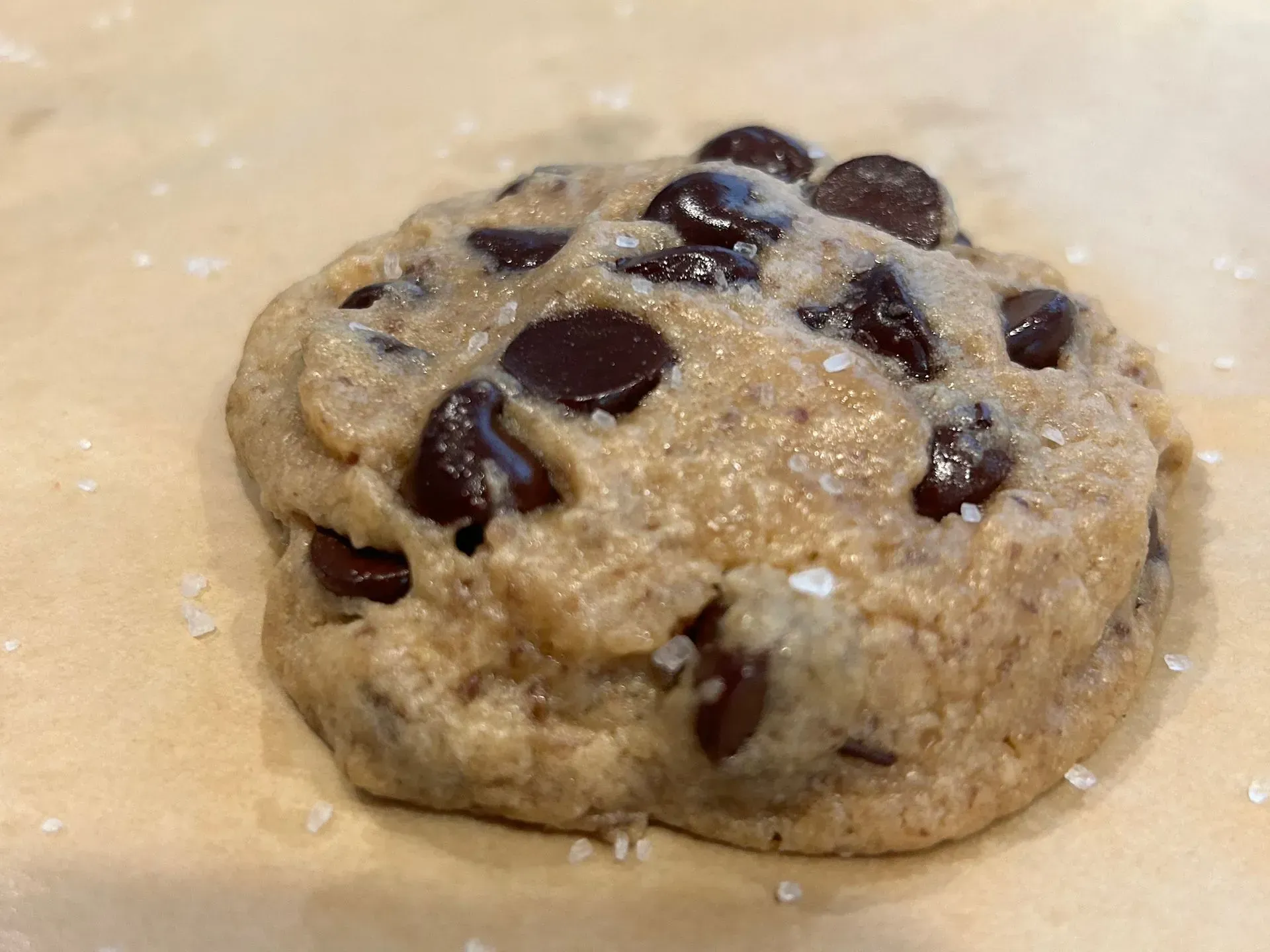 Chocolate chip cookie on parchment paper, sprinkled with salt.