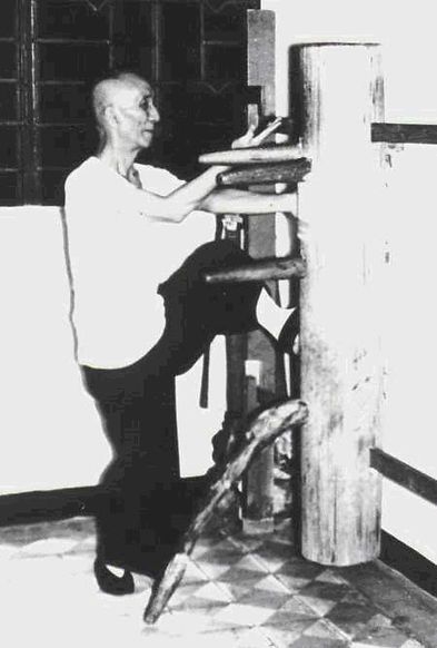 A man is kicking a wooden dummy in a black and white photo.