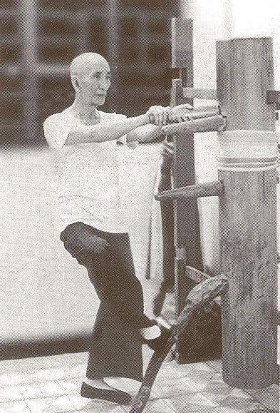 A man is practicing martial arts on a wooden dummy.