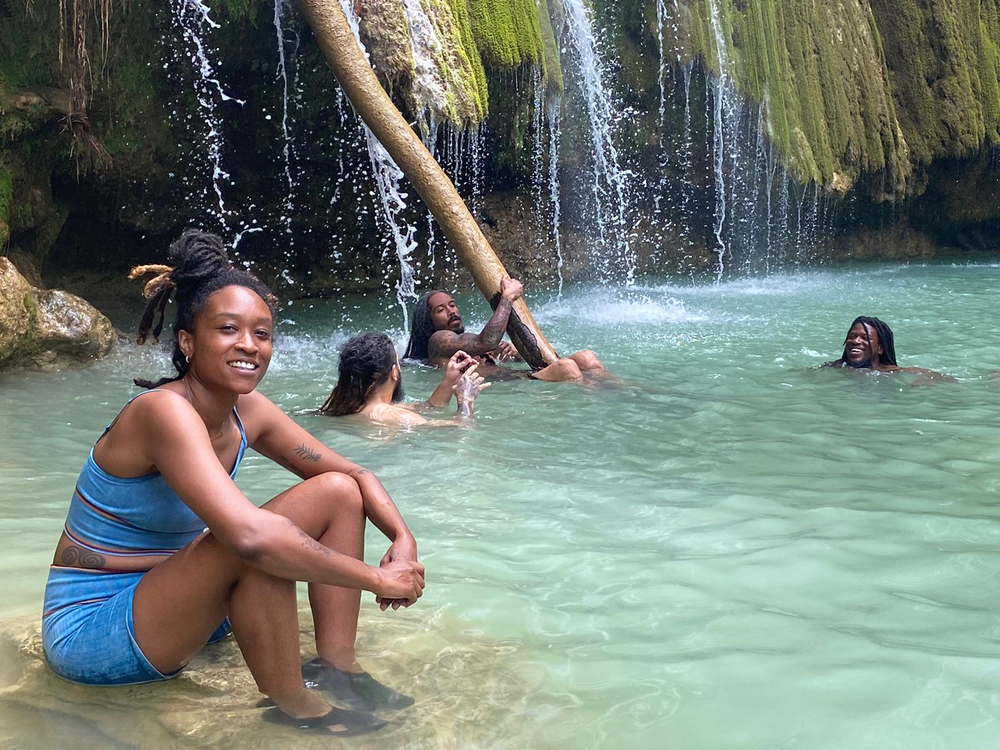 A woman is sitting in the water near a waterfall.