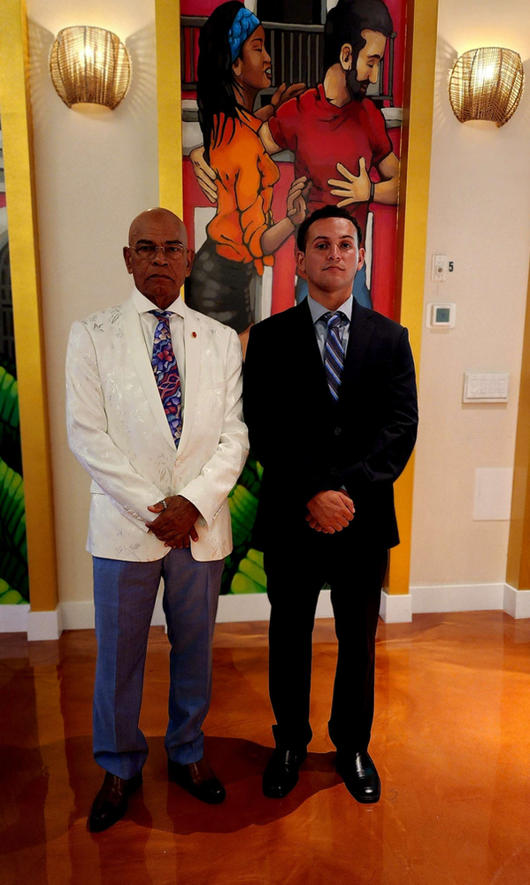 Two men are standing in front of a painting on the wall.