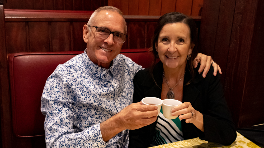 A man and a woman are sitting at a table holding cups of coffee.