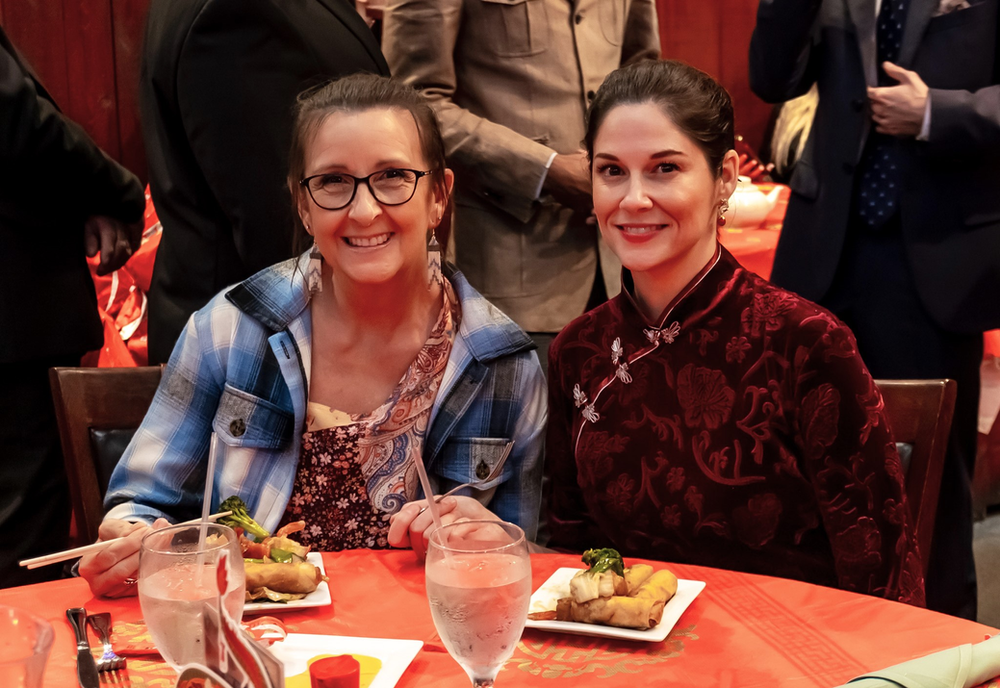 Two women are sitting at a table with plates of food and glasses of water.