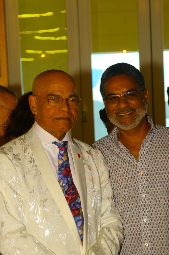 A man in a white suit and tie is shaking hands with another man.