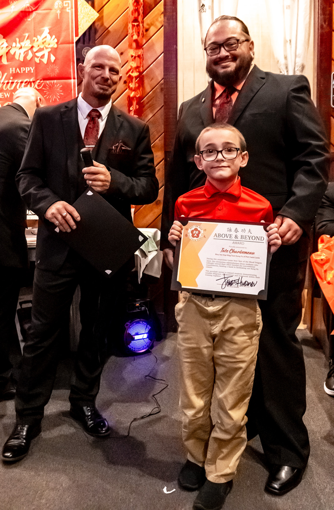 A young boy is holding a certificate while standing next to two men in suits.