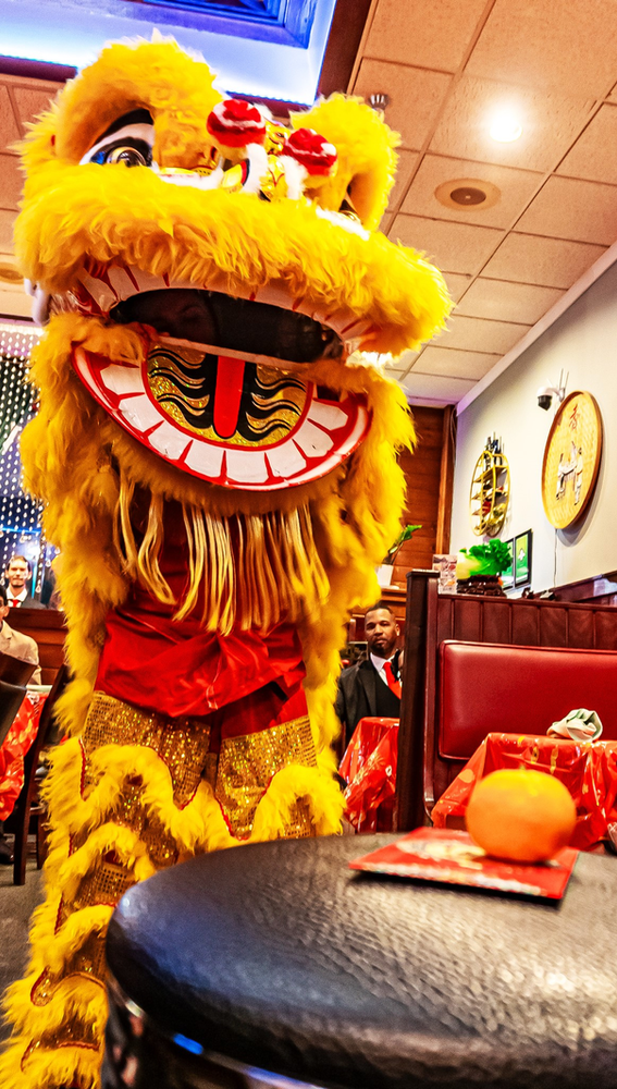 A lion costume is standing in a restaurant next to a table.