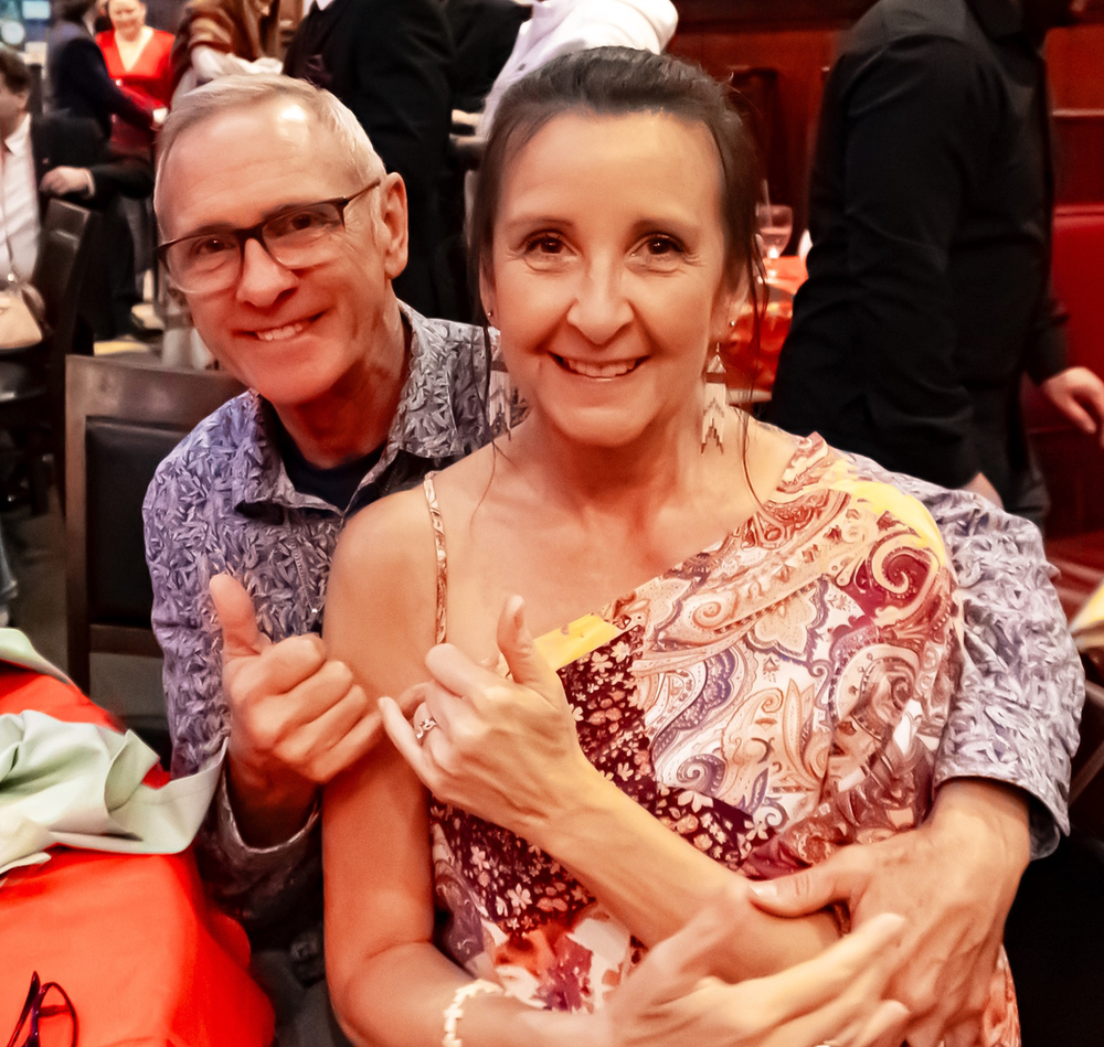 A man and woman are posing for a picture and the man is giving the woman a thumbs up