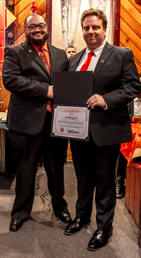 Two men in suits and ties are standing next to each other holding a certificate.