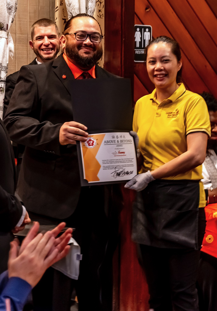 A man in a suit is holding a certificate next to a woman in a yellow shirt