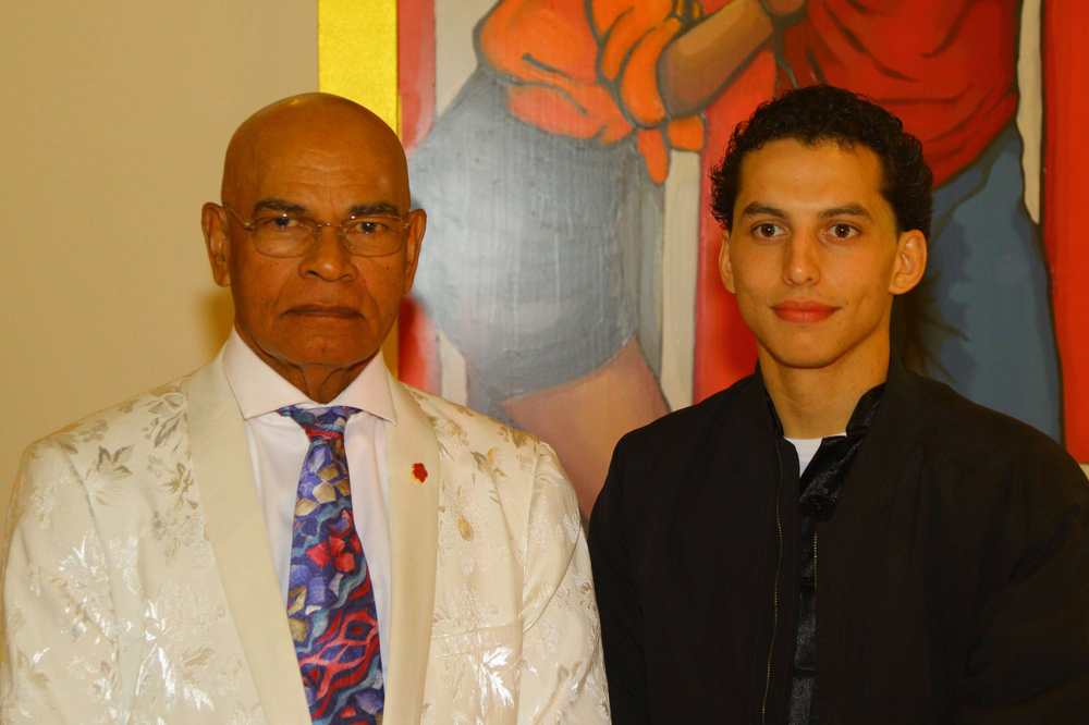 A man and a boy are posing for a picture in front of a painting.