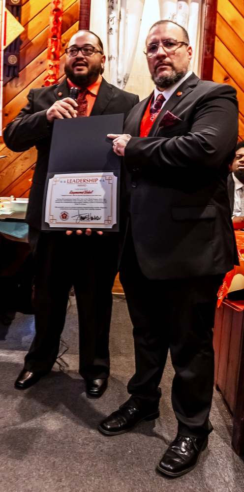 Two men in suits and ties are standing next to each other holding a certificate.