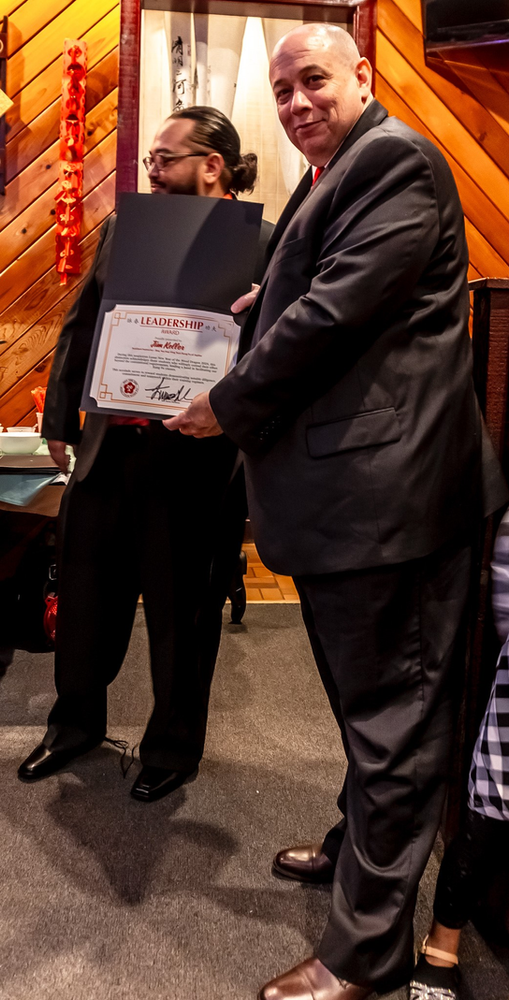 Two men in suits are standing next to each other holding a certificate.