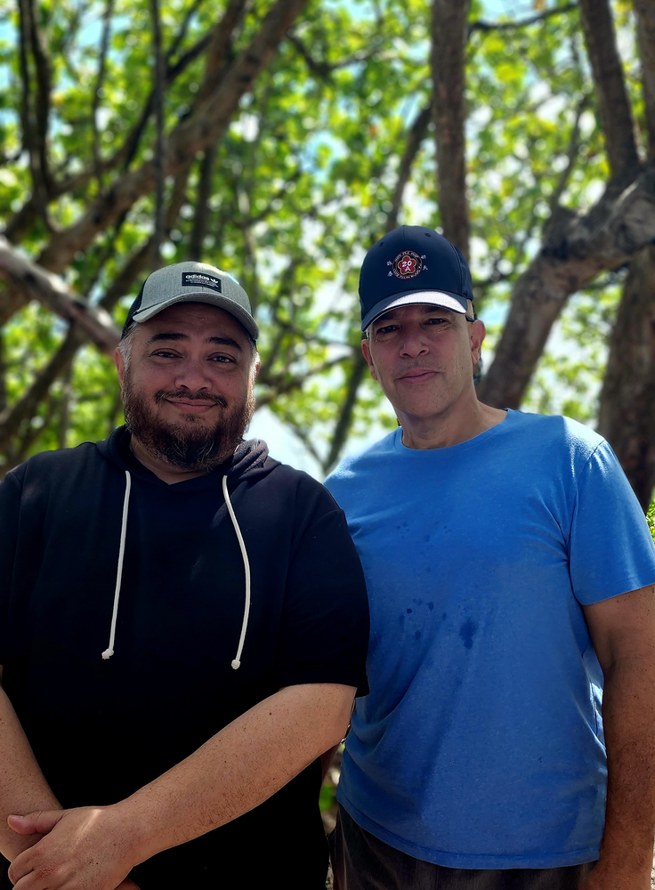 Two men are posing for a picture in front of a tree.