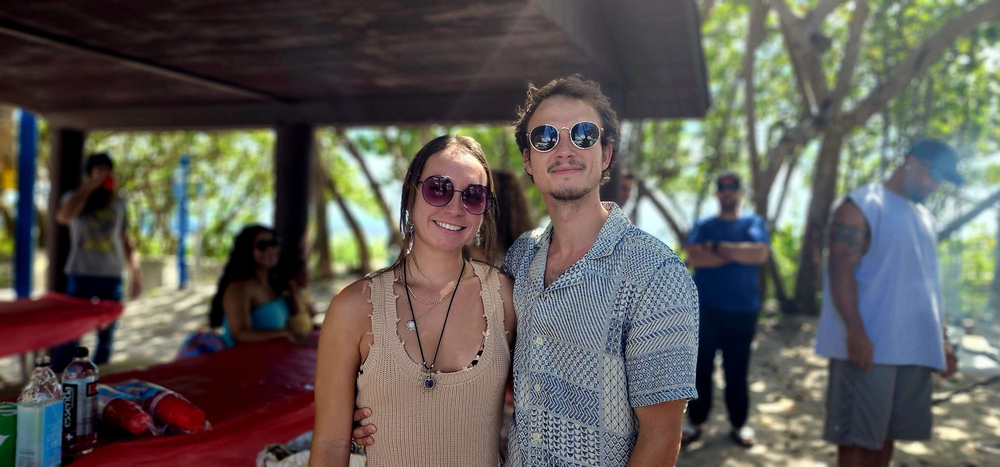 A man and a woman are posing for a picture on a beach.