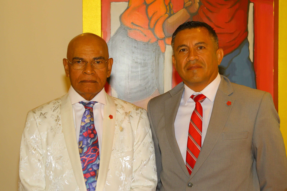 Two men in suits and ties are standing next to each other in front of a painting.