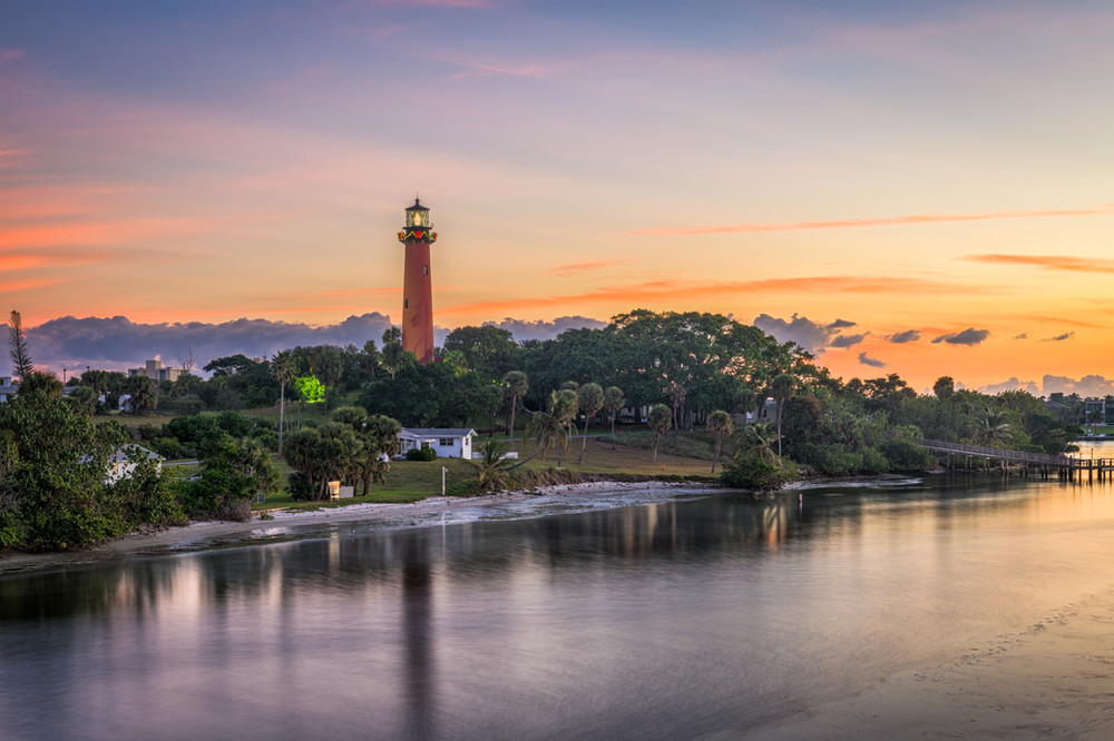 A lighthouse is sitting on top of a hill overlooking a body of water at sunset.