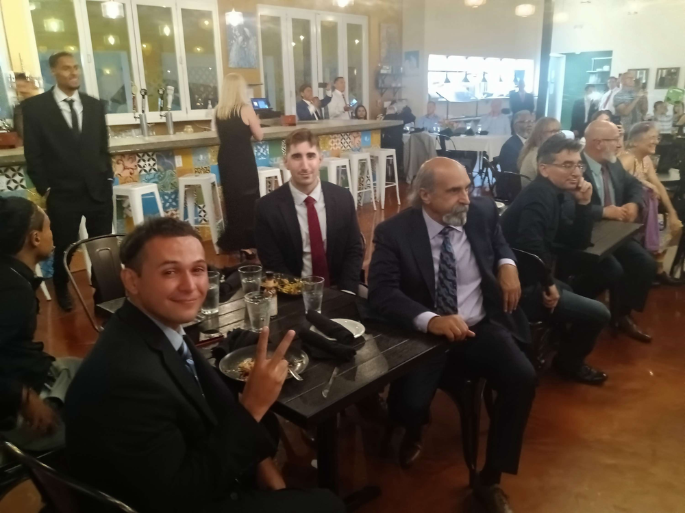 A group of men in suits and ties are sitting at tables in a restaurant