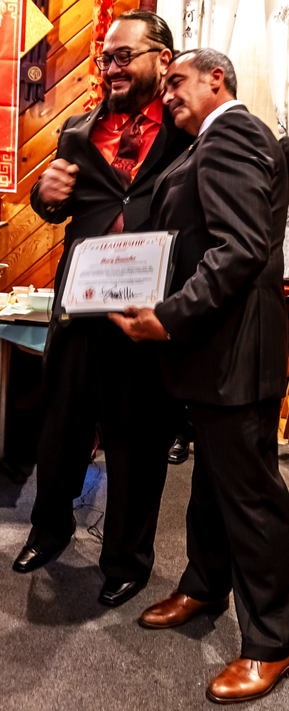 Two men in suits are standing next to each other holding a certificate.