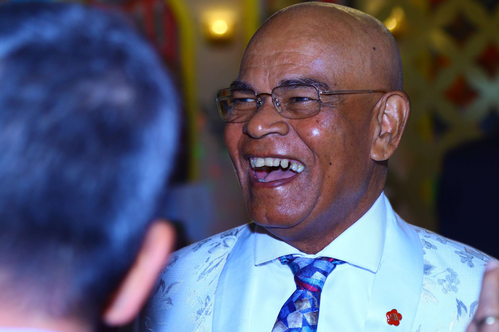 A bald man wearing glasses and a tie is laughing while talking to another man.