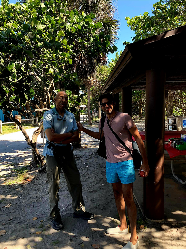 Two men are standing next to each other in front of a picnic table.