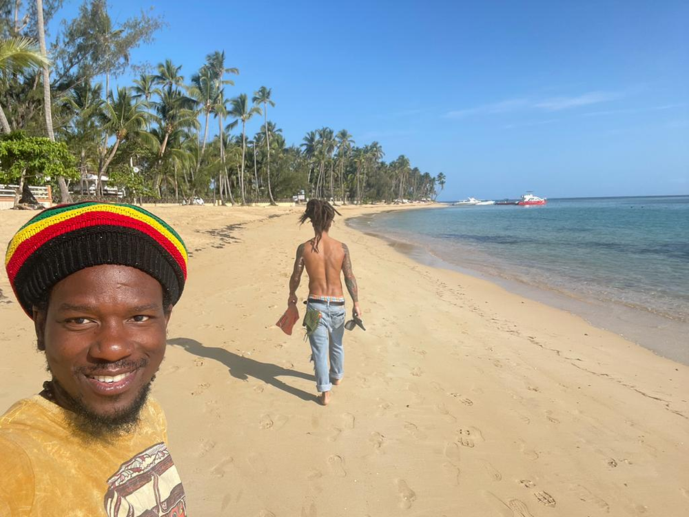 A man wearing a rasta hat is walking on a beach.