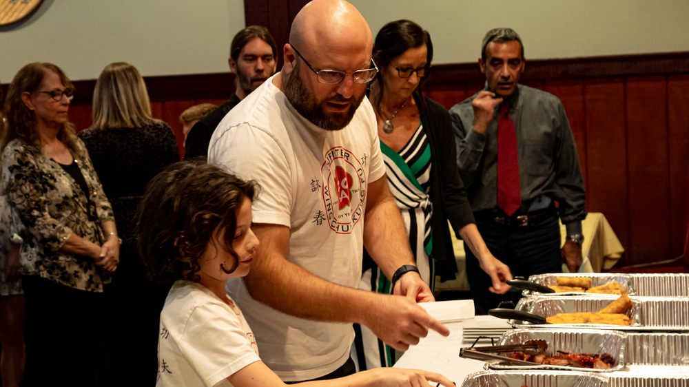 A man and a boy are standing in front of a buffet line.