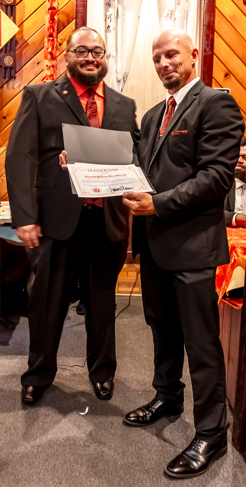 Two men in suits are standing next to each other holding a certificate.